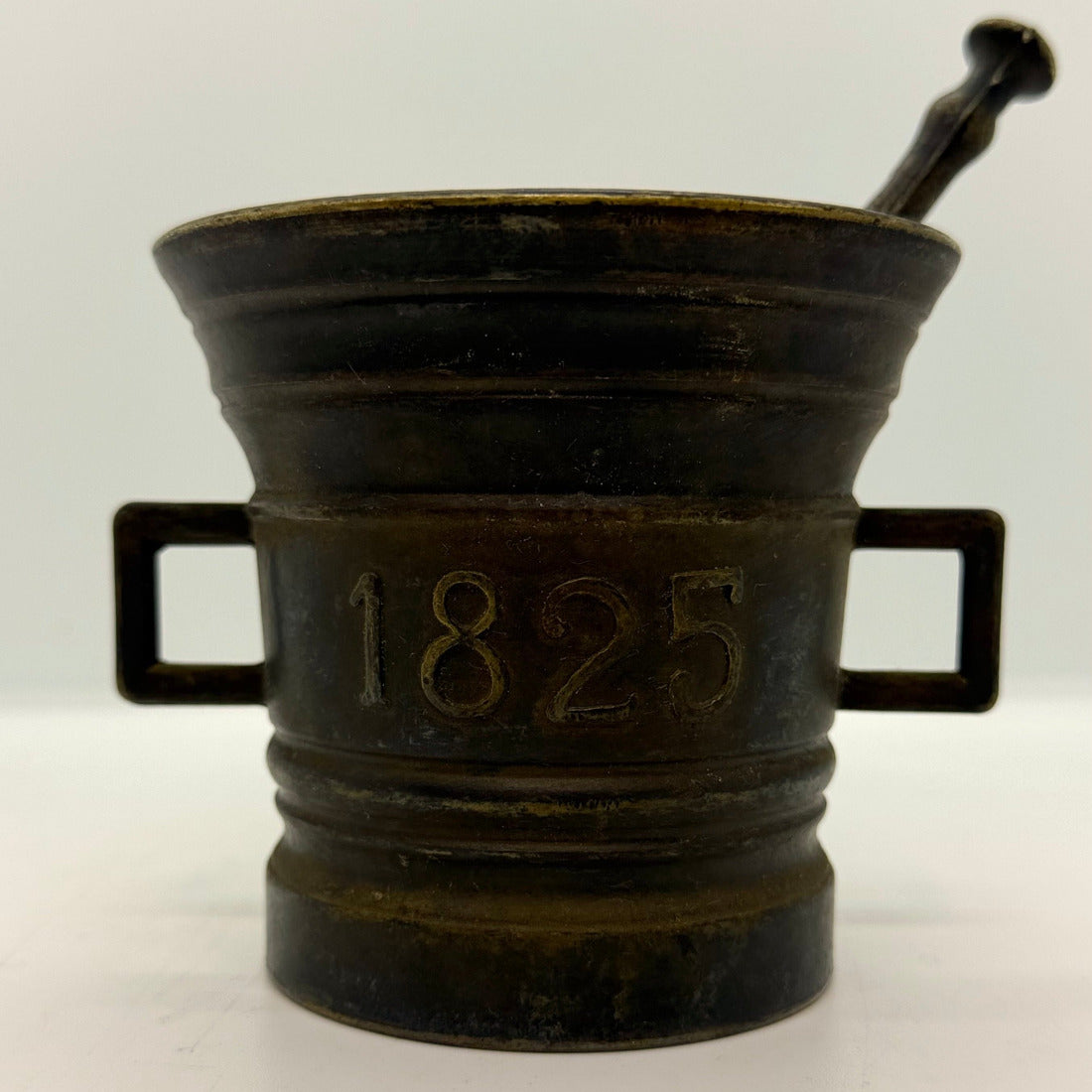 Antik mortel gjuten i brons med tillhörande stöt, märkt med årtalet 1825.