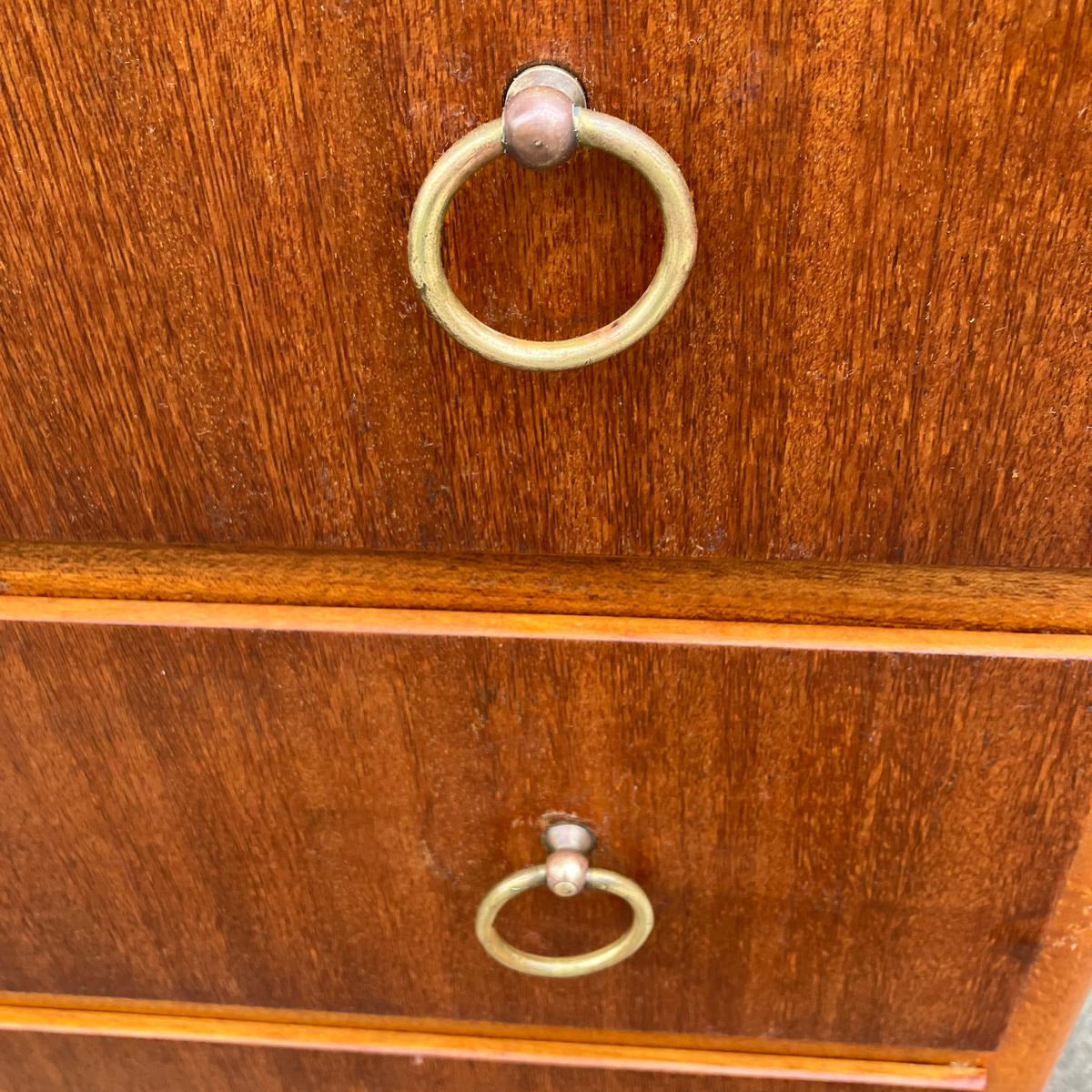 De dekorativa ringhandtagen i solid mässing ger en elegant kontrast till träets djupa ton och förstärker byråns tidlösa karaktär. 