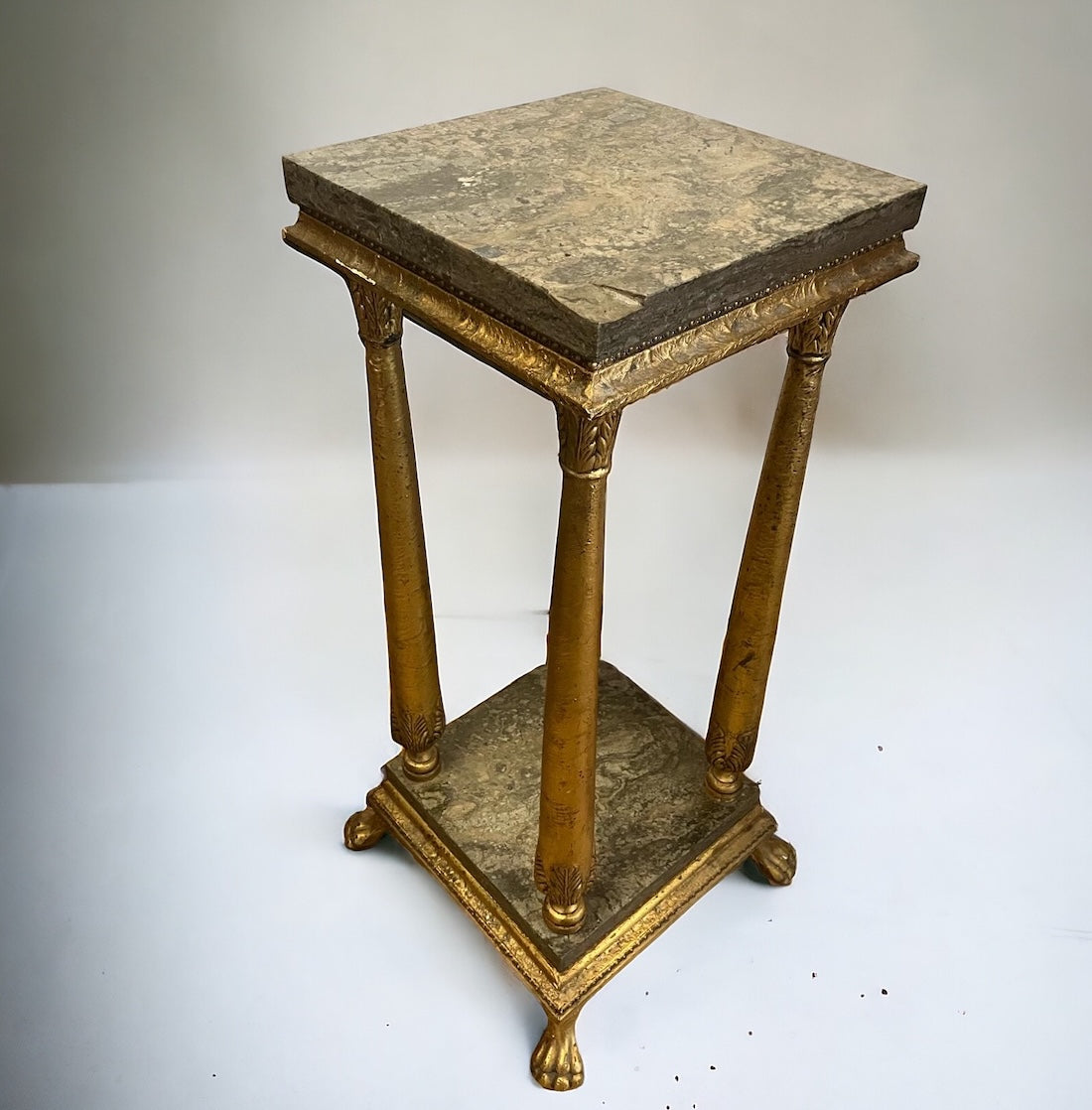 En stilig piedestal med klassisk elegans. Den är förgylld med ett rikt, varmt guld som fångar ljuset och framhäver de detaljerade ornamenten 
