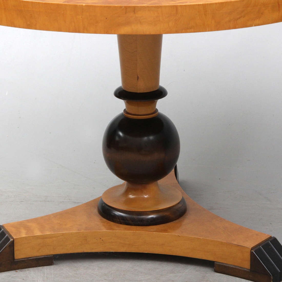 Pelarbordet vilar på en svarvad mittpelare och en stabil trefot med mörkare kontrasterande detaljer, vilket ger ett tidlöst och balanserat uttryck.