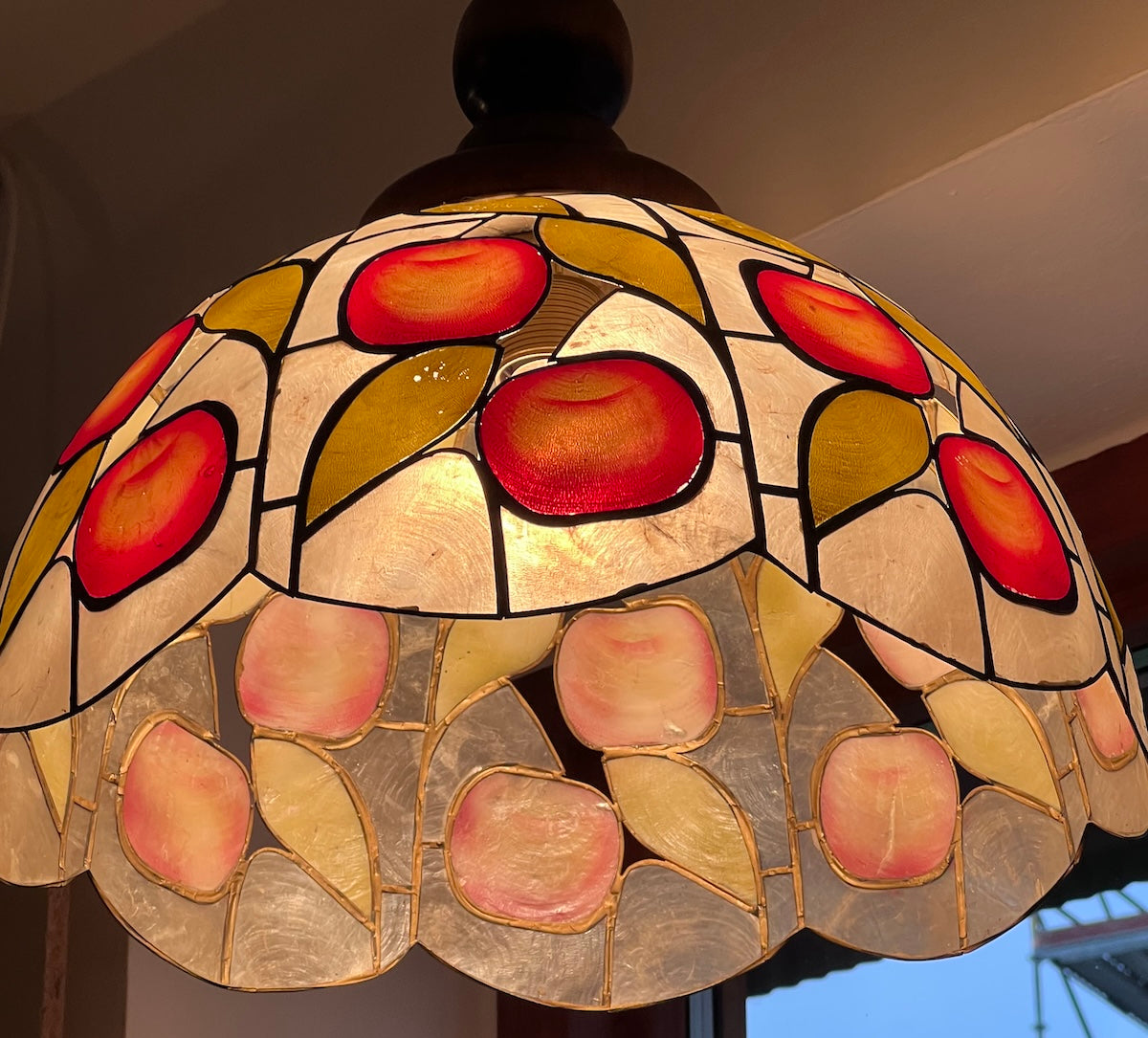 Lampan är inköpt i Frankrike och bär tydliga influenser av klassisk Art Nouveau–design, där de vackert färgade snäckbitarna samlas i ett organiskt mönster av röda frukter och guldfärgade blad. Den är i mycket fint skick, med detta dekorativa fruktmotiv och i äkta blyinfattning.